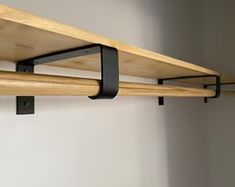 two wooden shelves with black metal brackets on the top and bottom, against a white wall