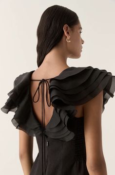 a woman wearing a black dress with ruffles on the back