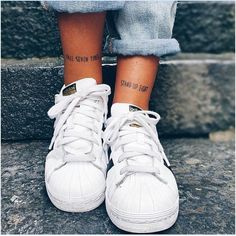 a person with tattoos on their legs standing on some steps and wearing white tennis shoes