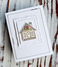 a card with a house on the front and two red flowers in the middle, sitting on top of a wooden table