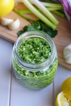 a jar filled with green pest next to lemons and onions