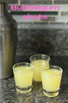 three shot glasses filled with yellow liquid sitting on a counter next to a shaker