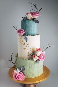 a three tiered cake decorated with flowers and leaves on a gold plated stand