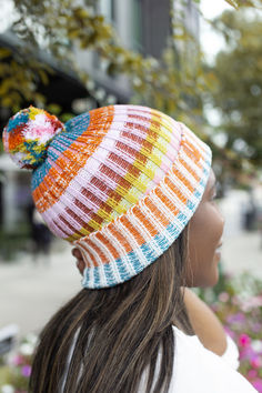 a woman wearing a multicolored knitted hat with pom - poms