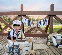 a little boy dressed in a sailor outfit sitting on a deck next to other items