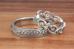 two silver rings with green stones sitting on top of a wooden table