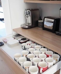 a drawer with cups and coffee mugs on it in a kitchen next to a toaster