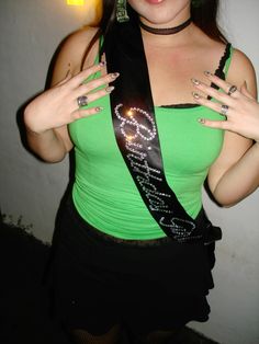 a woman wearing a green shirt and black skirt with her hands on her chest, posing for the camera