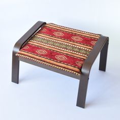 a small wooden stool with a red and green striped seat cover on it's back