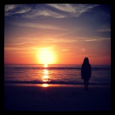 a woman standing on top of a beach next to the ocean under a cloudy sky