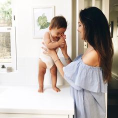 a woman holding a baby up to her face while standing on top of a counter