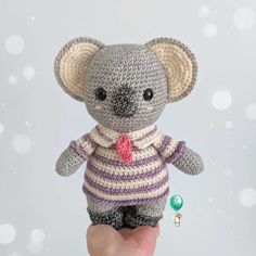 a hand holding a small crocheted stuffed animal in a sweater and bow tie