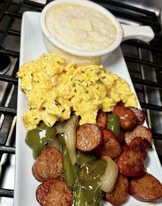 a white plate topped with eggs and sausage next to a bowl of soup on top of a stove