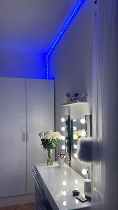 a white vanity with blue lights and flowers on it's counter top in front of a mirror