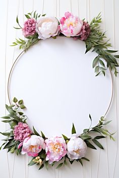 a white circle with pink flowers and greenery around it on a wooden background, top view