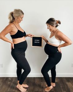 two women standing next to each other in black and white outfits, one is holding a sign