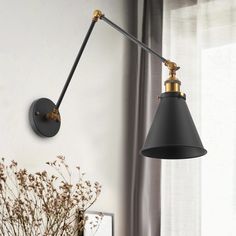 a black and gold wall light next to a vase with dried flowers on the table