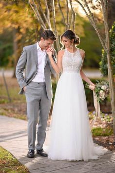 a bride and groom standing on a path in front of trees with their hands together