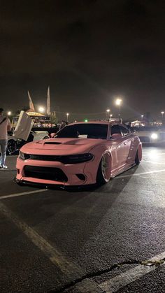 two cars parked in a parking lot at night with people standing around and looking at them