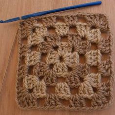 a crocheted square with a blue needle