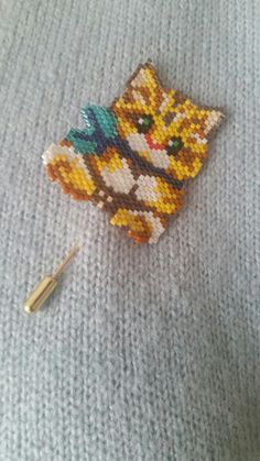 a pin with a cat on it sitting on top of a blanket next to a knitting needle