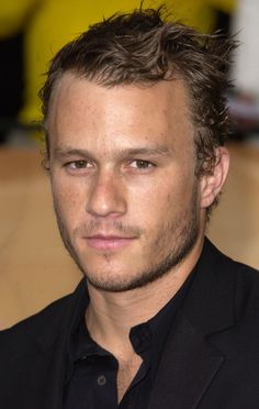 a close up of a person wearing a suit and black shirt with his hair in the air