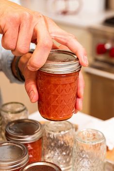 a person is holding a jar with some food in it on a table next to other jars