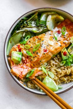 a bowl filled with rice, meat and veggies next to chopsticks