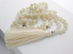 "Finding Balance 108 Bead Mala  Creamy Moonstone Tassel Necklace  Hand Knotted Meditation Tool and Crystal Healing // Unisex Jewelry Moonstone also opens the heart and assists in the acceptance of love. It relieves the feeling of hopelessness, and helps provide balance. It stabilizes emotions and helps create harmonious relationships. It is the stone of love.  The stones are genuine cream colored moonstone. The spacer beads are silver plated.   All of our malas have 108 beads and are handmade and knotted in between each bead. Each mala is vegan and animal free, strung on nylon thread with a handmade polyblend tassel. It will come in a box ready to be given as a gift if needed with muslin storage bag and stone properties as well.  This mala is 100% handmade right here in the US by a team of Mala Bead Necklace, 108 Mala Beads, Meditation Gifts, Finding Balance, 108 Bead, Yoga Gifts, Moonstone Necklace, Moonstone Jewelry, Unisex Jewelry