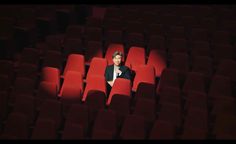 a woman sitting in the middle of a row of red chairs with her hands behind her head