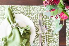 a place setting with green napkins and flowers on the side, along with silverware