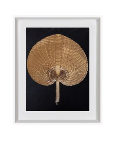 a bamboo fan hanging from the ceiling in a white frame on a black wall behind it