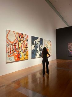 a woman standing in front of three paintings on the wall at an art gallery with hard wood flooring