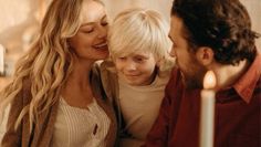 a woman and two boys sitting next to each other in front of a lit candle