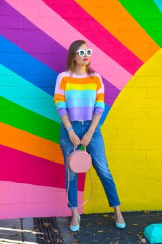 a woman standing in front of a colorful wall wearing sunglasses and holding a frisbee