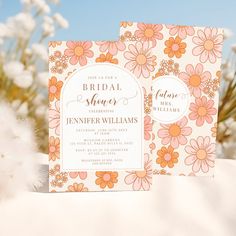 two wedding cards with flowers on them sitting in front of some white fluffy grass and blue sky