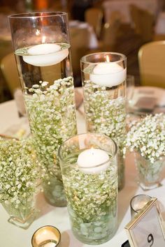 three tall vases filled with baby's breath flowers and candles on a table