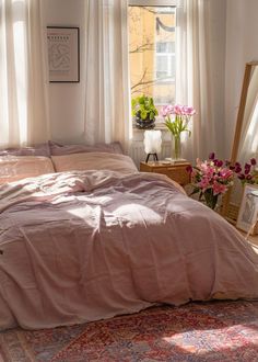 an unmade bed with pink sheets and pillows in a bedroom next to a window