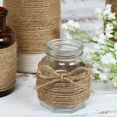 three jars with twine and rope tied around them on a white wooden table next to flowers