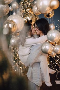 two women hugging each other in front of a christmas tree with gold and silver ornaments