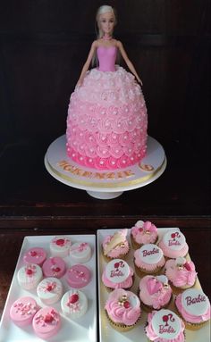 a barbie doll cake and cupcakes are on display