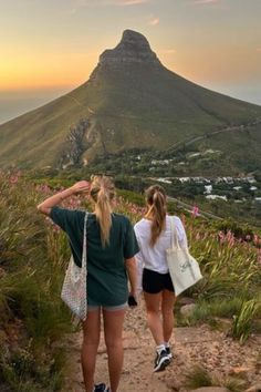 two young women walking up a hill towards the ocean with a mountain in the background