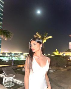 a woman standing on top of a roof next to a palm tree at night with the moon in the background