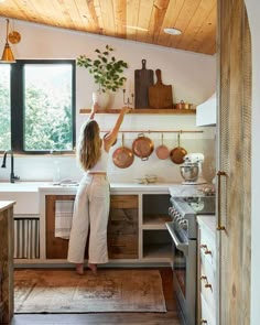 a woman standing in a kitchen with pots and pans on the wall above her head