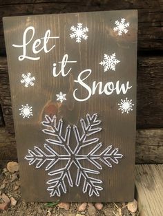 a wooden sign that says let it snow with white snowflakes on the front