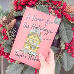 a person holding up a book in front of a wreath with berries and pine cones