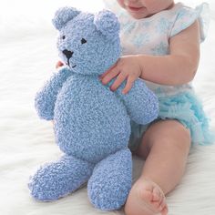 a baby girl is holding a blue teddy bear