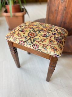 an old wooden bench with a colorful upholstered seat and back rest in front of a potted plant