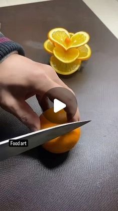 a person cutting an orange with a knife on top of it next to some fruit