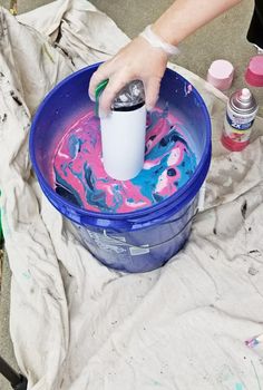 a person is painting in a bucket with pink and blue paint on it's surface